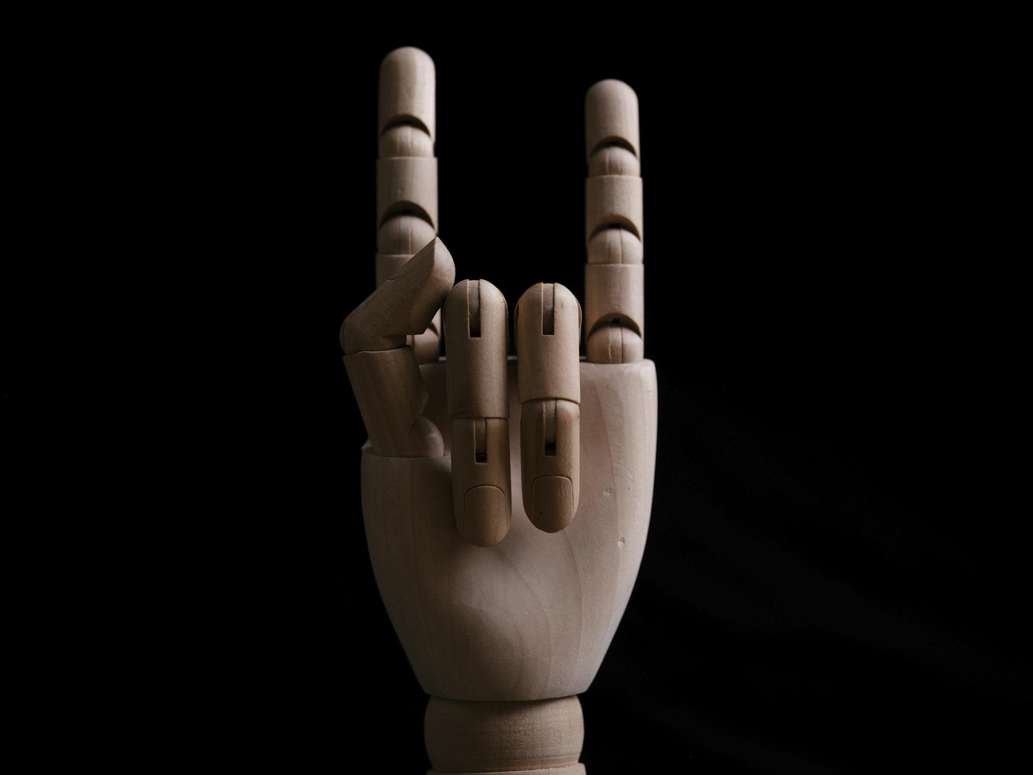 A wooden mannequin hand posing in a rock gesture symbol against a dark background.