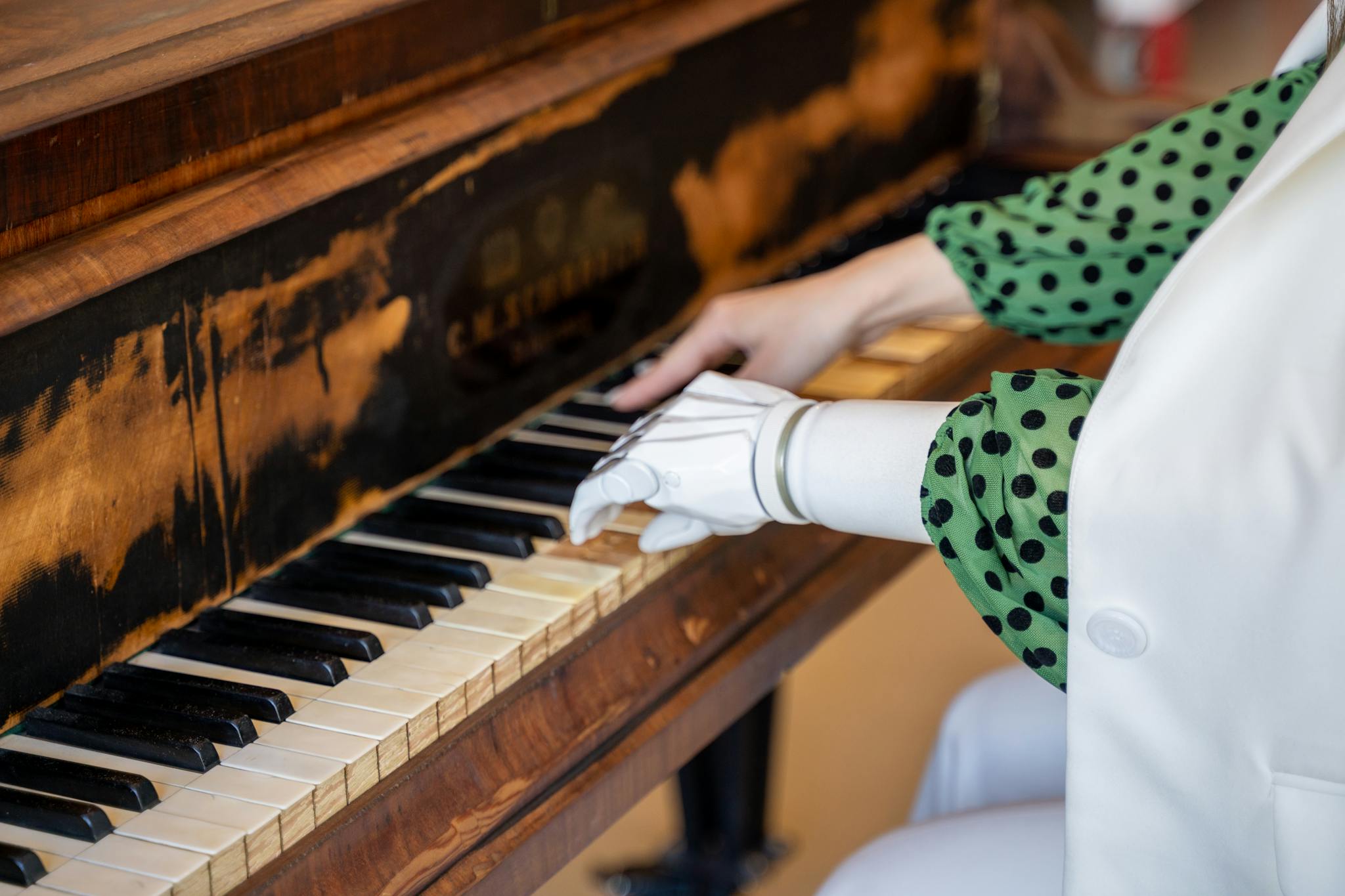Close-up of a person with a prosthetic hand playing a vintage piano.