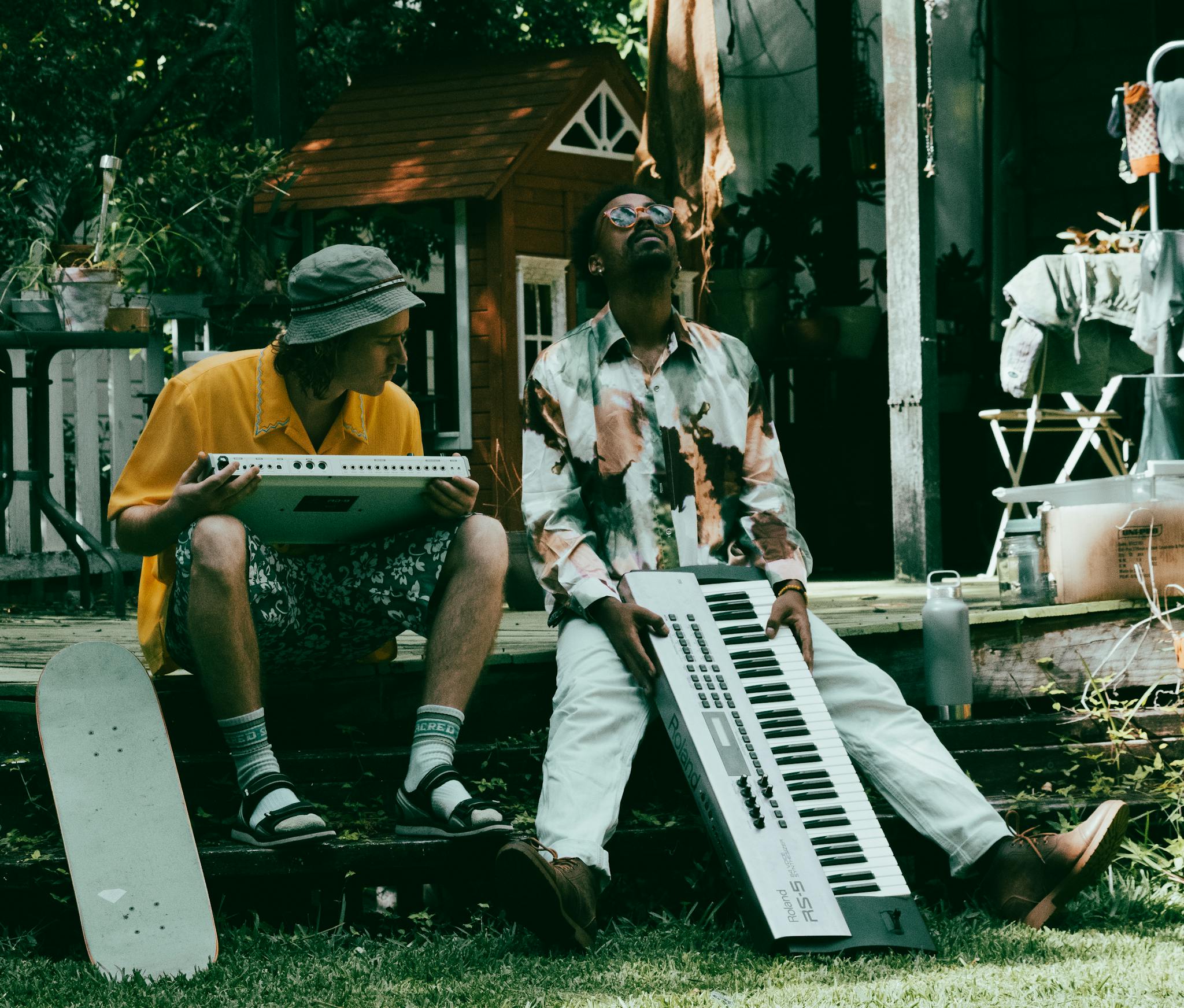 Two men playing keyboards outdoors, enjoying a relaxed music session in a garden setting.
